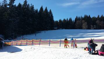 A snowy ski slope with a colorful fence and trees in the background.