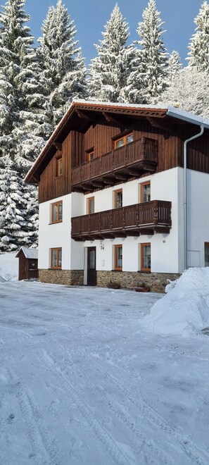 A multi-story wooden building with balconies, surrounded by snow-covered trees. - Pension Pek (Kubova Hut)