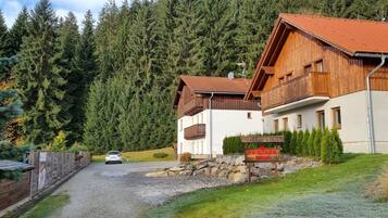 A wooden building with a red-tiled roof, a sign reading "Pension Park," and a gravel driveway leading to a parked car.