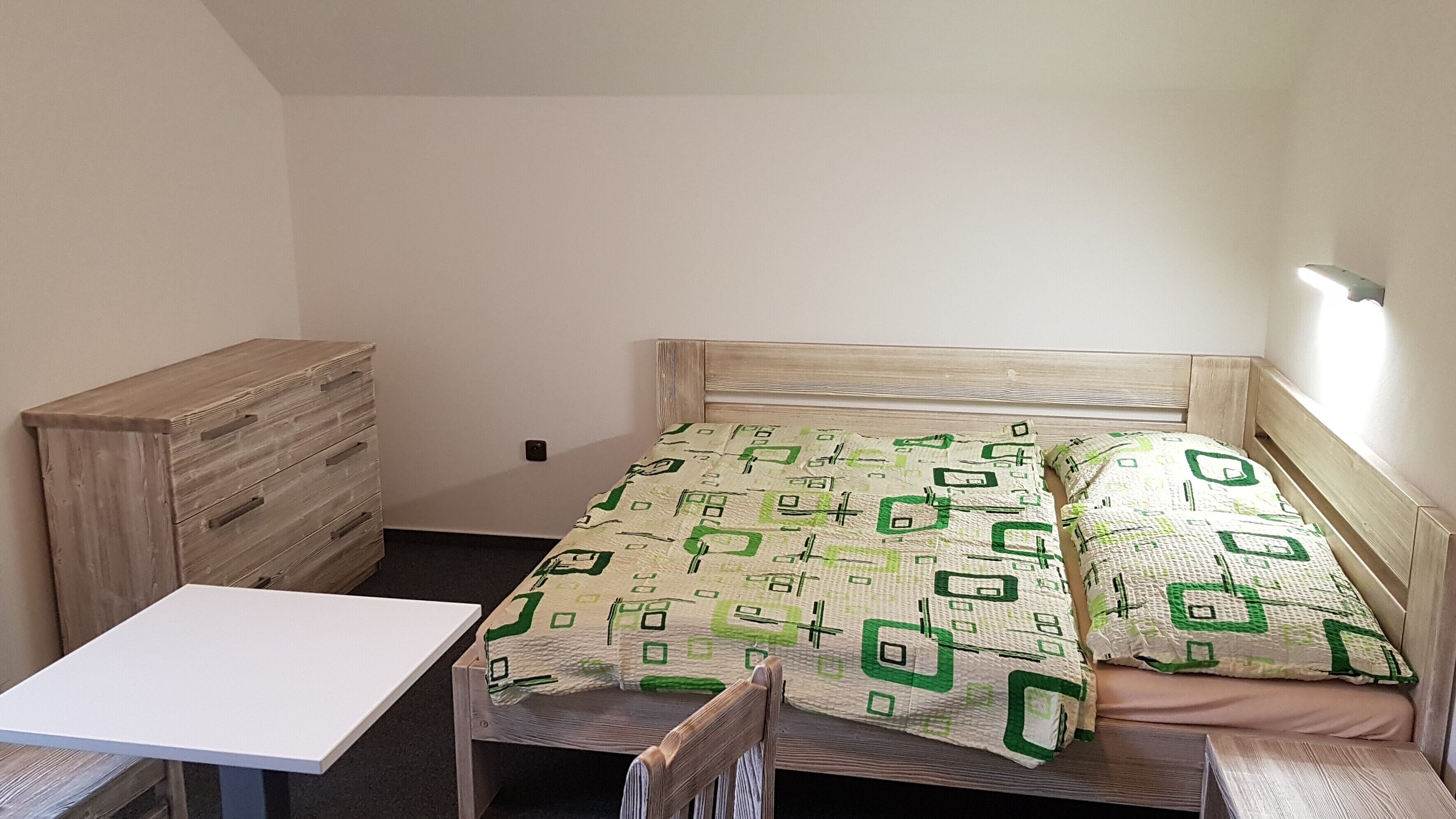 Une petite pièce simple, avec un lit, une commode en bois et une petite table.