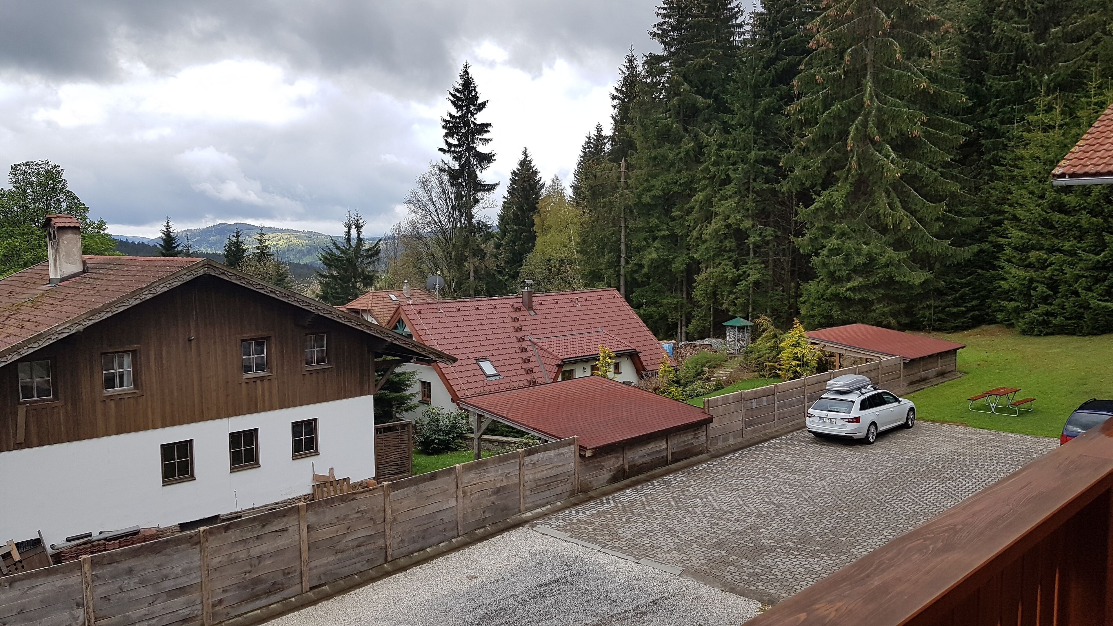 A residential area with wooden houses, a paved driveway, and a car parked near a picnic table.
