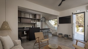 A modern living room with a sofa, two wicker chairs, a coffee table, and a kitchen area with a staircase leading to an outdoor area. - Bianco Villa - Eve (Rhodes)