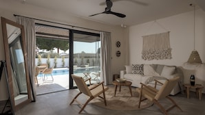 A spacious living area with a sliding glass door leading to a pool, a ceiling fan, and a round coffee table. - Bianco Villa - Eve (Rhodes)