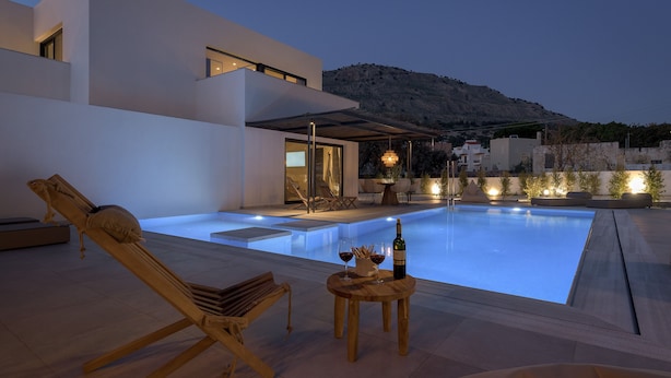A modern outdoor pool area with a lounge chair, a table with drinks, and a mountain backdrop. - Bianco Villa - Eve (Rhodes)