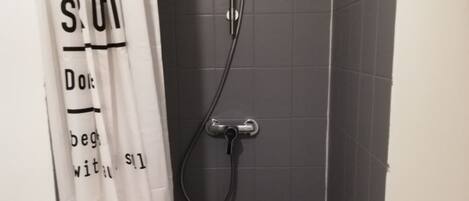 A shower with a handheld showerhead and a wall-mounted faucet.
