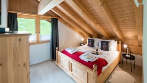 Ein Schlafzimmer mit Holzboden und schrägen Wänden, ausgestattet mit einem Bett mit weißen Leinen, einer roten Decke und einem Nachttisch mit Lampe.
