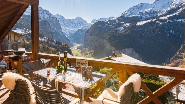 Eine Holzterrasse mit Tisch und Stühlen mit Blick auf ein gebirgiges Tal.