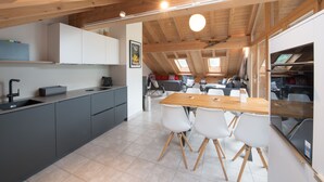 Eine moderne Küche mit Holzbalkendecke, grauen Schränken und einem Essbereich mit weißen Stühlen.