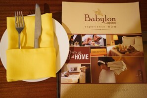 A brochure for Babylon Capital hotel with a dining setup including a fork, knife, and napkin. - Babylon Capital (Raipur)