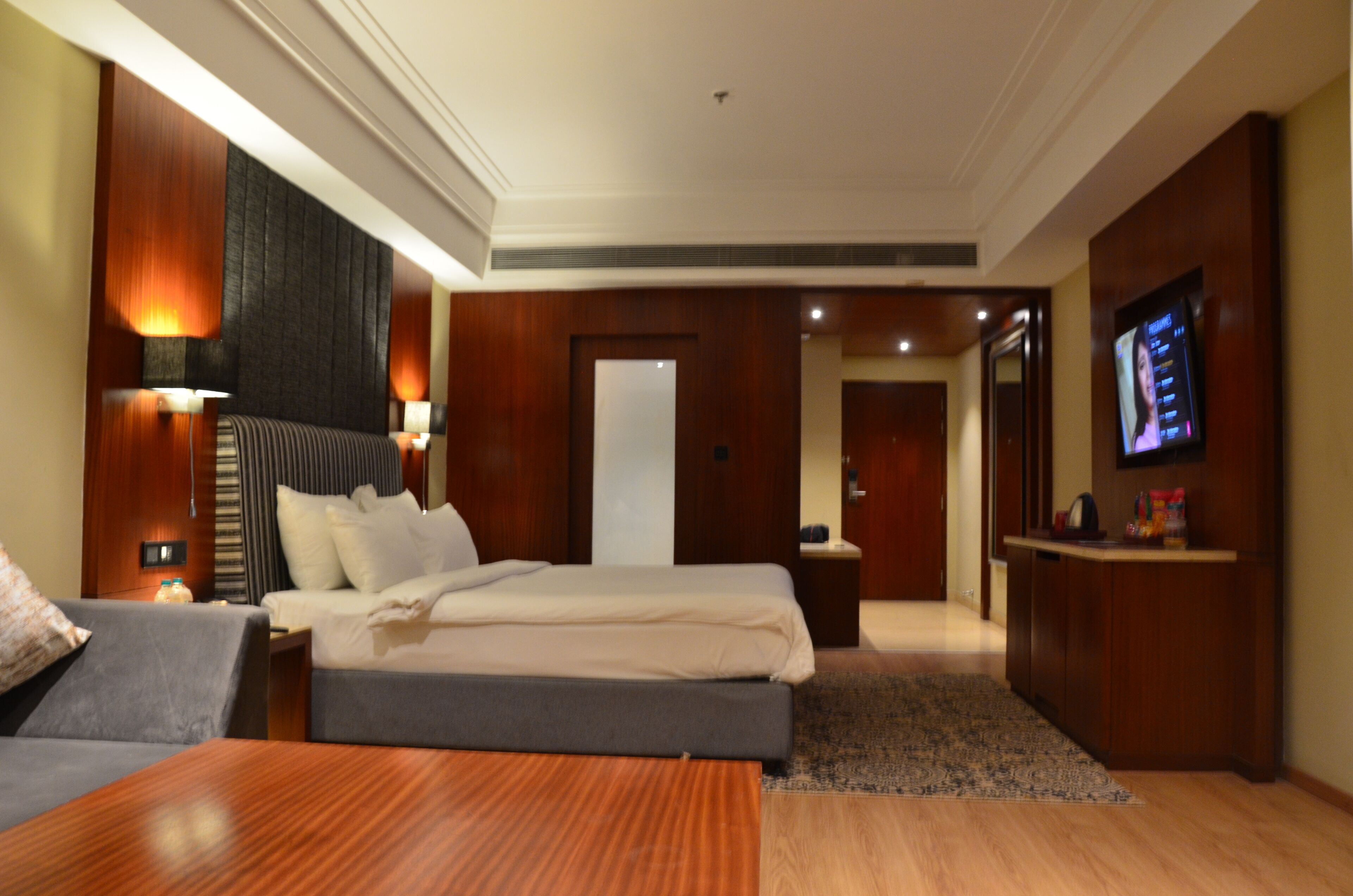 A hotel room with a large bed, bedside tables, a TV, and a sofa.