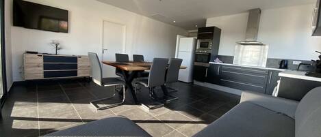 Une cuisine moderne avec un coin repas, comprenant une grande table et des chaises, un four encastré et un four à micro-ondes.