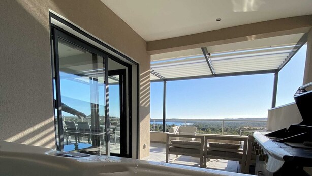 Un moderno espacio de spa con una bañera de hidromasaje, una puerta de cristal que da a una zona de estar al aire libre y vistas al paisaje.