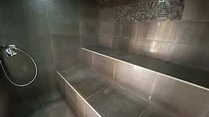 A modern bathroom with dark tiles, a shower area, and a bench. - Pinarello sea view — 3-bed, heated pool 29°C, walk to beach, private spa (3) (Zonza)