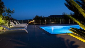 Una piscina con sillas de descanso y vistas a las montañas al atardecer.