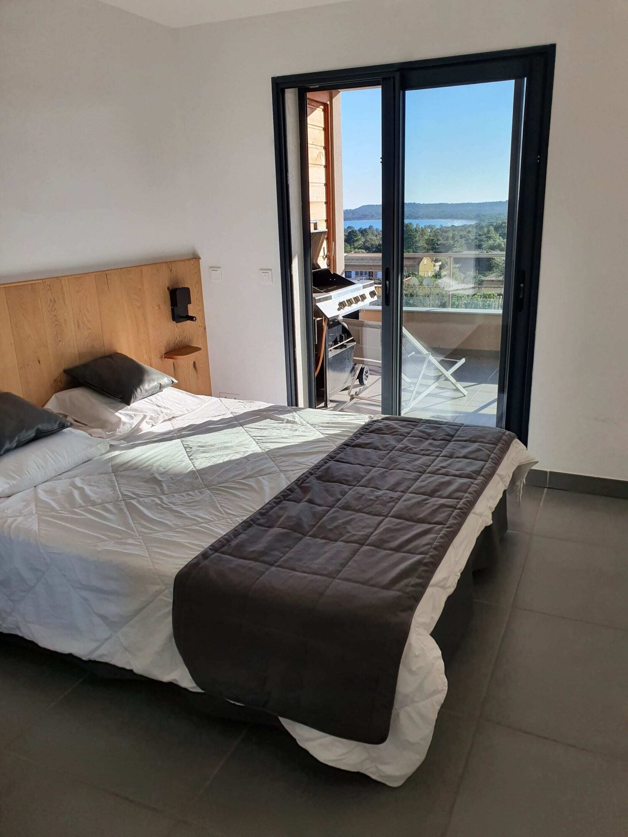 A bedroom with a bed, a wooden headboard, a sliding glass door to a balcony, and a view of the outdoors.