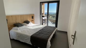 Un dormitorio moderno con una cama grande, cabecera de madera y vistas al exterior a través de un ventanal corredero.
