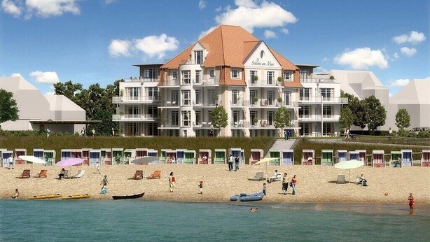 Un hôtel doté de nombreux balcons, situé en bord de mer et offrant des chaises longues et des parasols sur la plage.