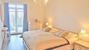 Une chambre à coucher avec un grand lit, un lustre, une table de chevet, un bureau et une fenêtre avec des rideaux.