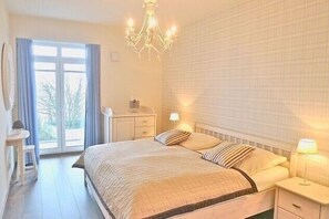 Ein Schlafzimmer mit einem großen Bett, einer Kandelaber, einem Nachttisch, einem Schreibtisch und einem Fenster mit Vorhängen.