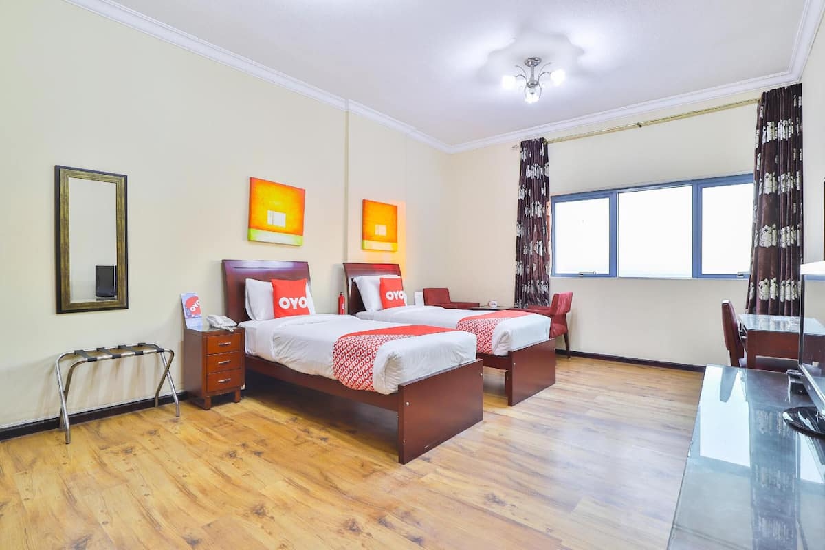 Ein Hotelzimmer mit zwei Betten, einem Schreibtisch, einem Stuhl, einem Heizkörper und einem Fenster mit Vorhängen.