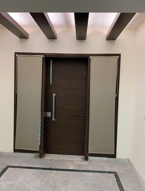 Enter through the door with a metallic handle, flanked by two panels, into a space with a skylight above.