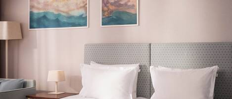 Una habitación de hotel con cama, dos cuadros en la pared, una mesita de noche con lámpara y un cabecero estampado.