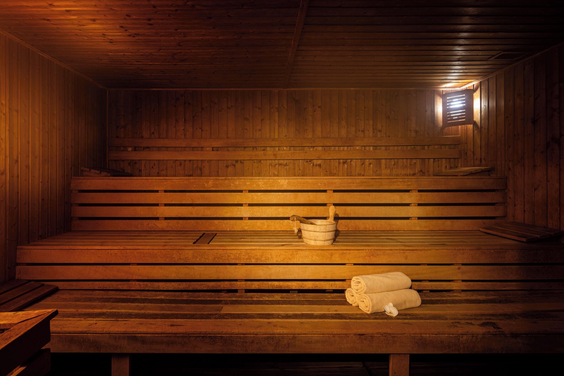Un sauna avec des bancs en bois, un seau et des serviettes.