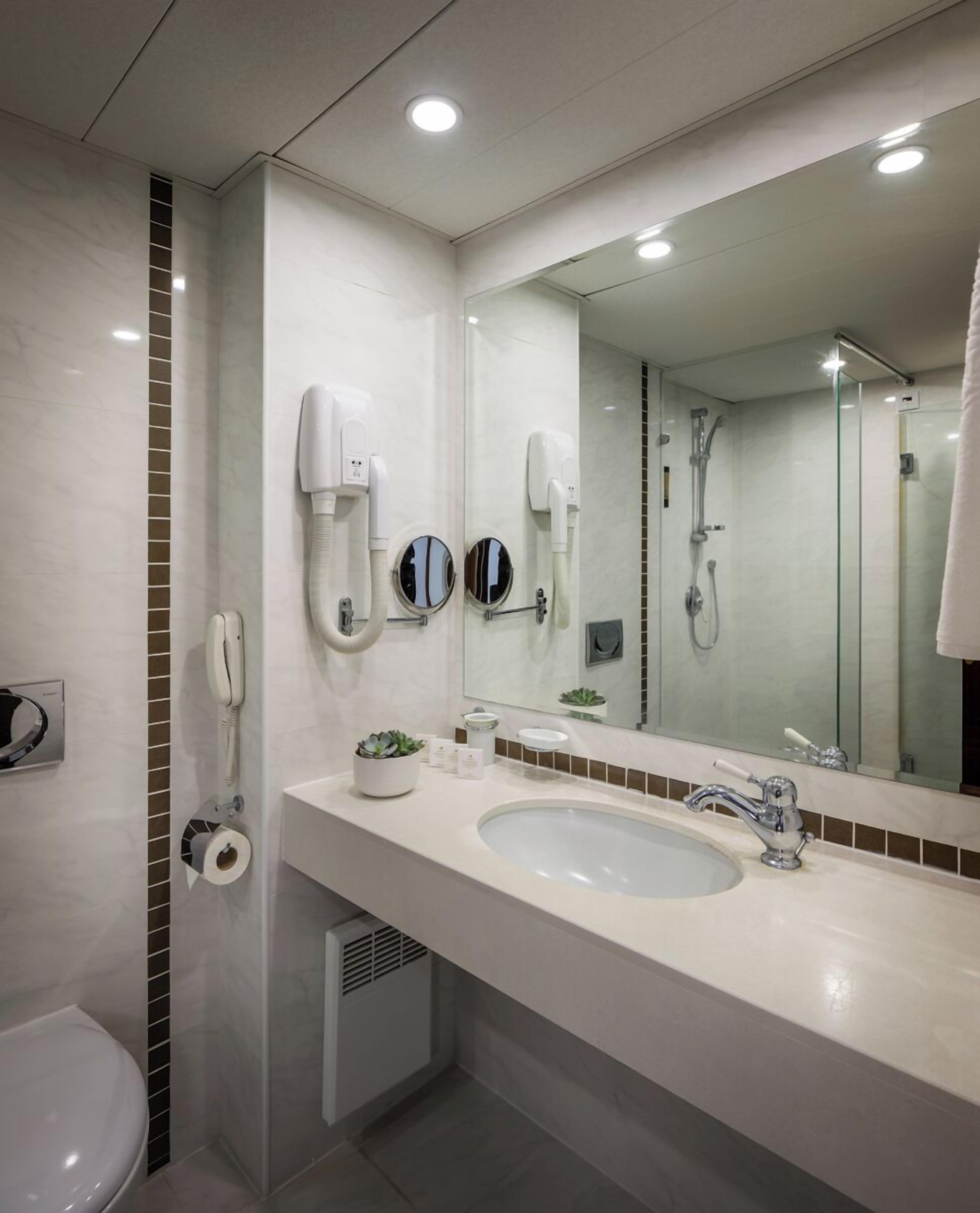 A modern bathroom with a large mirror, a sink, a toilet, and a shower.