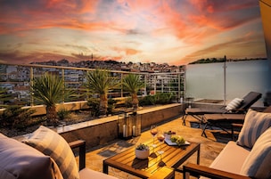 Terraço no telhado com vista para o pôr do sol, mobiliário ao ar livre e paisagem urbana ao fundo.