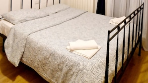 Een enkel bed met een bedovertrek met patroon en kussens, een wandlamp en een raam met gordijnen.