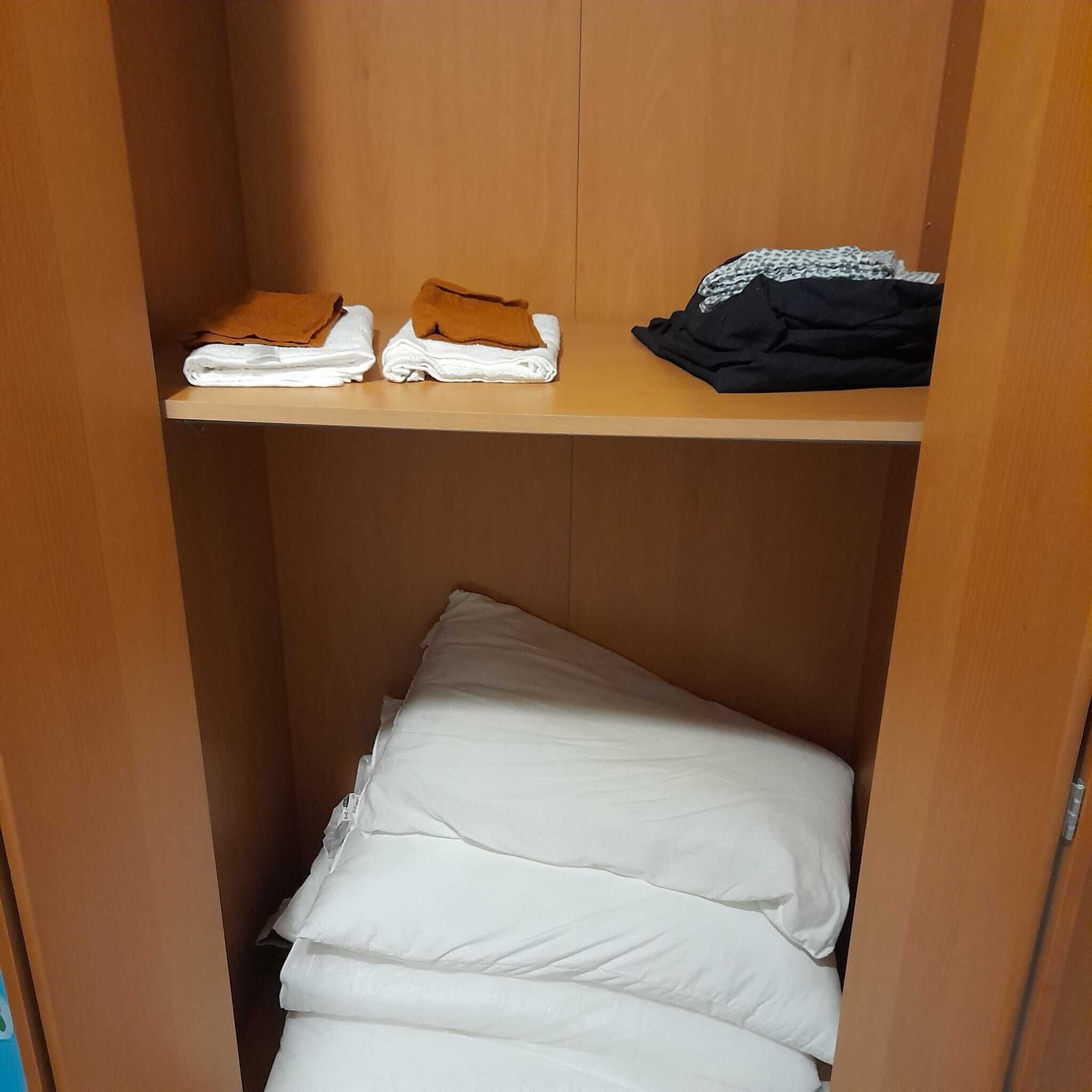 Een houten garderobe met een plank waarop opgevouwen handdoeken en een kledingstuk liggen.