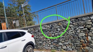 Een witte auto geparkeerd naast een stenen muur met een metalen hekwerk erboven.