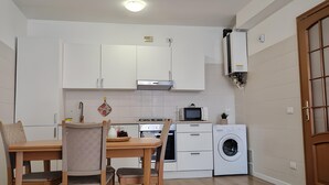 Een moderne keuken met witte kasten, een eettafel met stoelen, een magnetron, een wasmachine en een plafondlamp.
