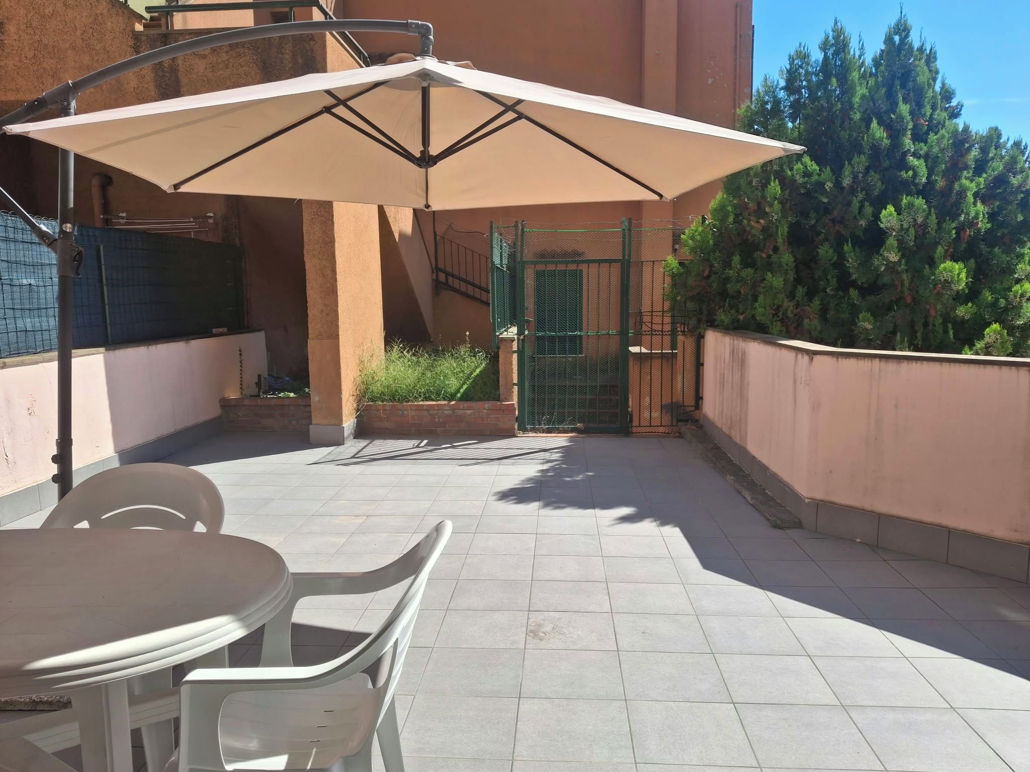 A patio area with a table and chairs, a large umbrella, and a green gate.