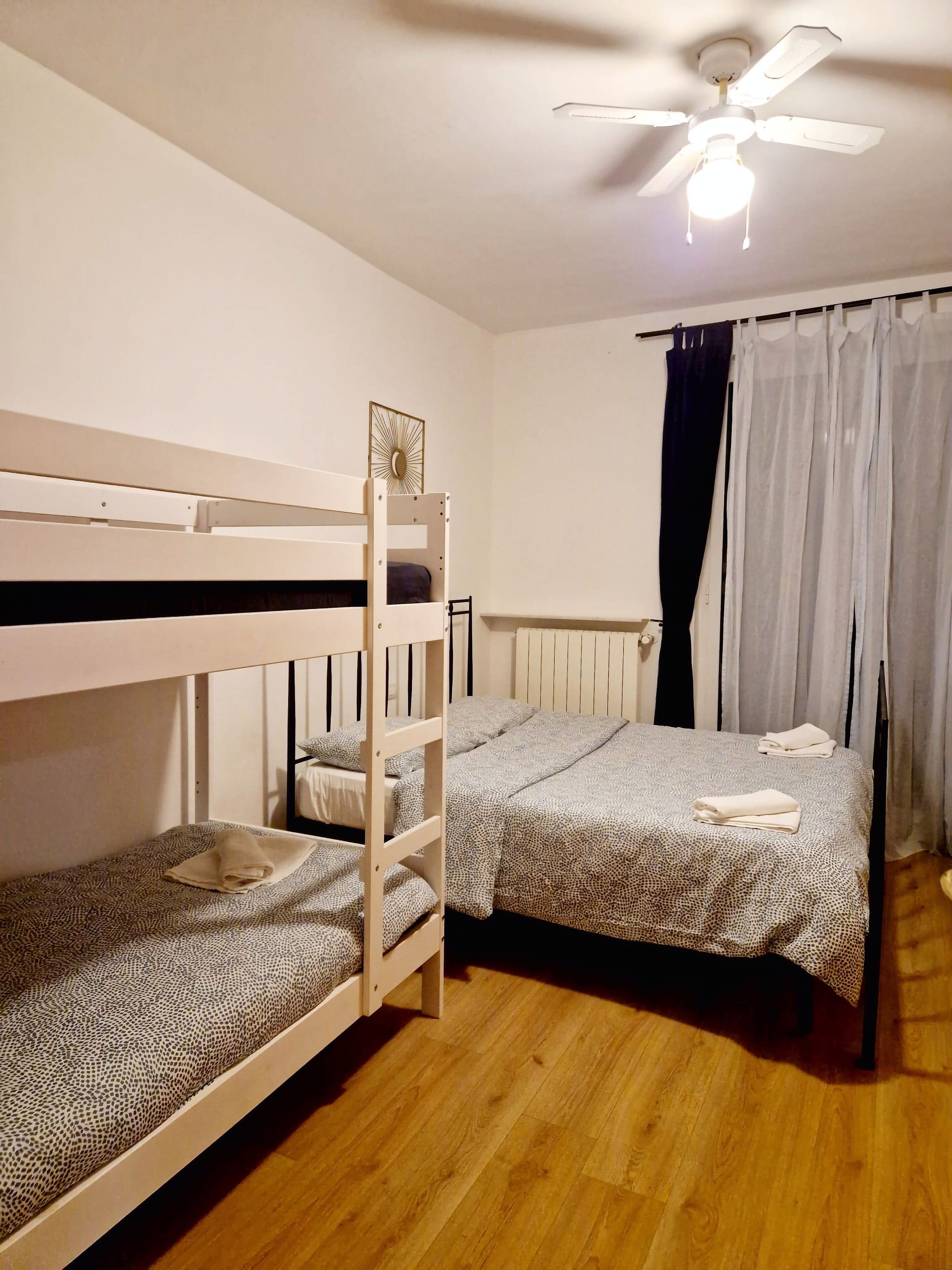 A room with two bunk beds, a ceiling fan, and a window with curtains.