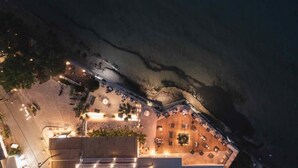 Vista aérea de un hotel frente a la playa con zonas de estar al aire libre y una piscina.