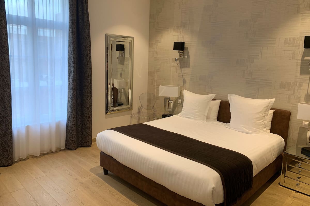 Une chambre d’hôtel avec un grand lit, un miroir, deux lampes de chevet, une table de nuit et une fenêtre avec des rideaux.