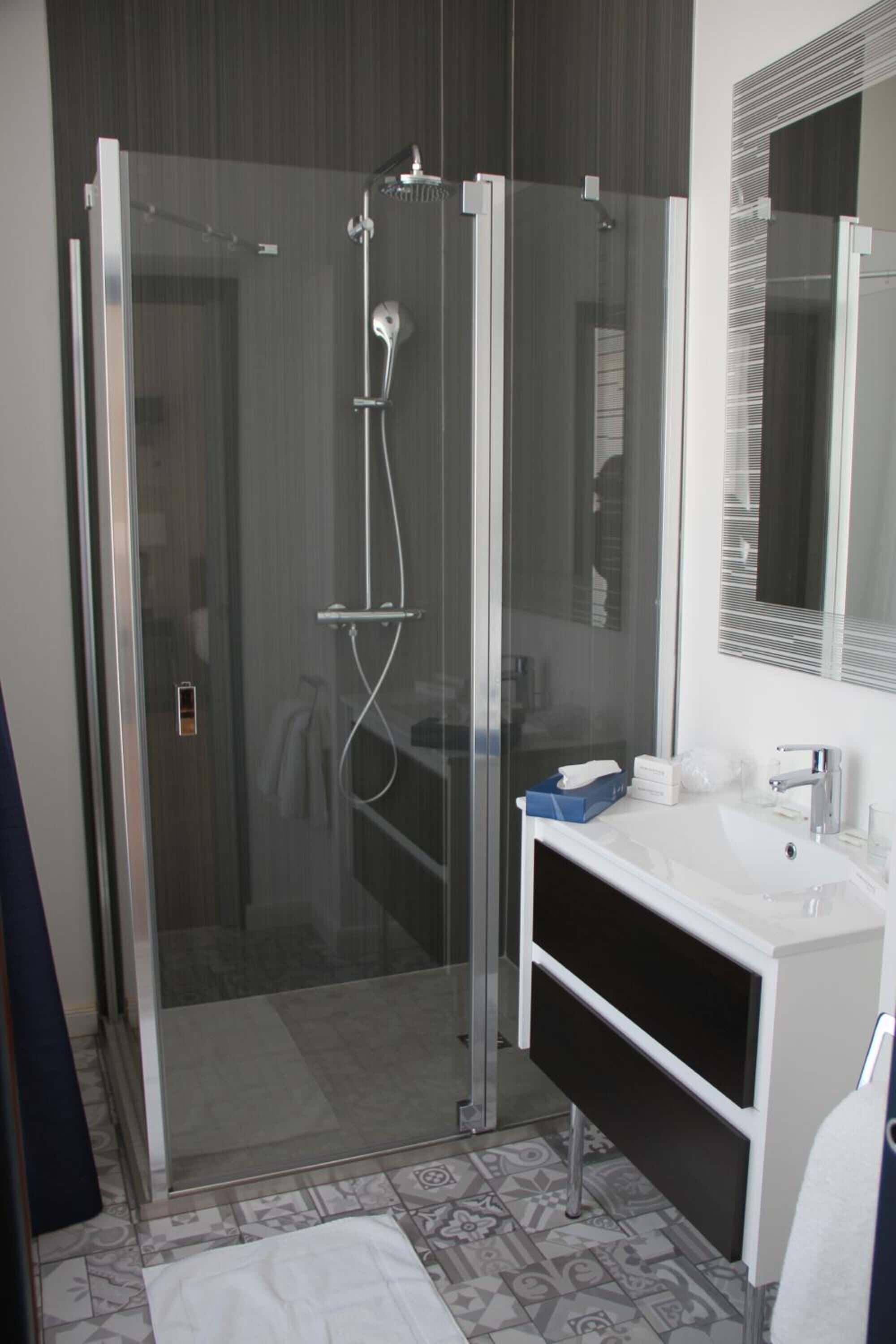 A modern bathroom with a glass-enclosed shower, a white sink, and a large mirror.