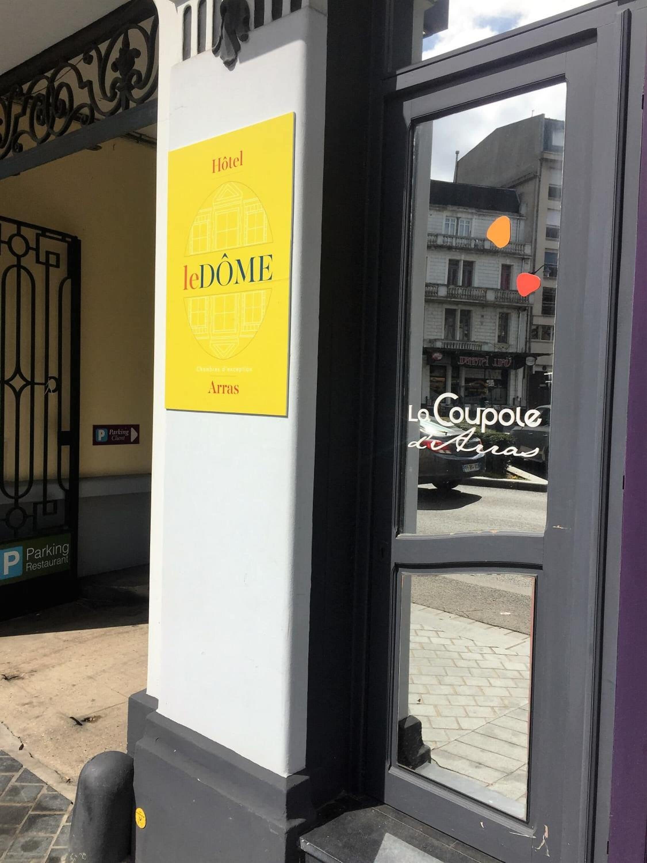 A hotel entrance with a sign reading "le DOME Hotel" and a "Parking Restaurant" sign.
