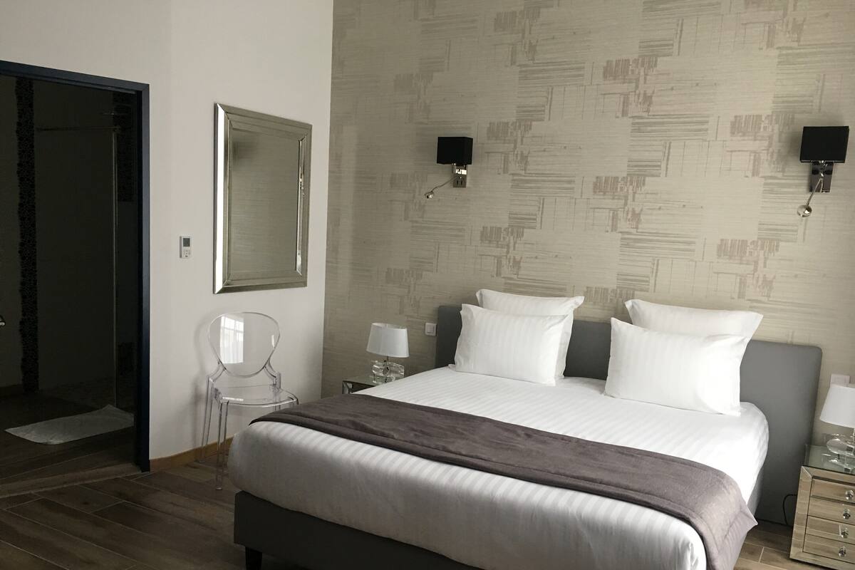 Une chambre à coucher avec un grand lit, une table de chevet avec une lampe, une chaise, un miroir et un haut-parleur fixé au mur.
