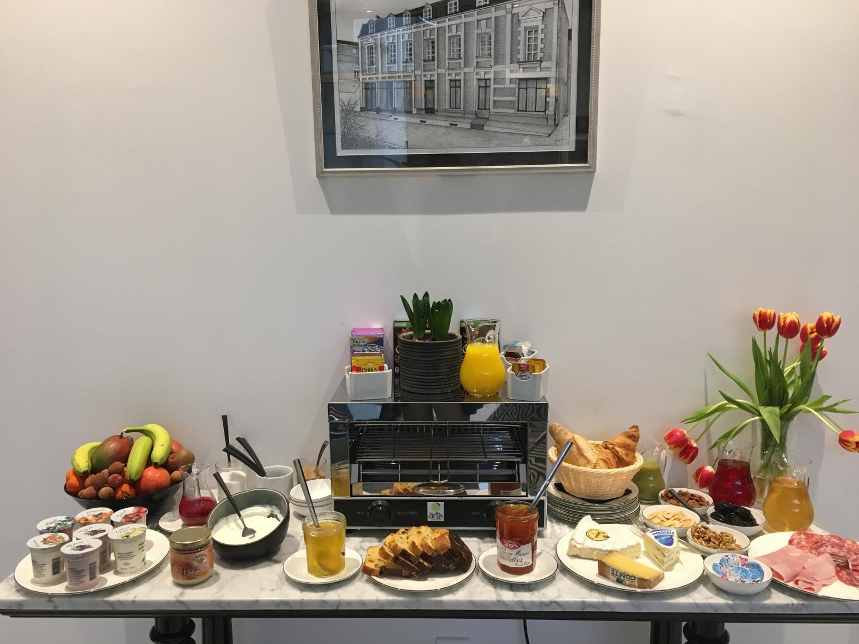 A breakfast buffet with various food items, a selection of drinks, and a framed architectural drawing on the wall.