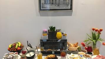 A breakfast buffet with various food items, a selection of drinks, and a framed architectural drawing on the wall.
