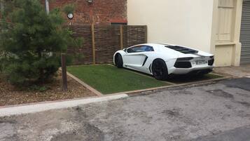 A white sports car parked in a driveway with a small lawn and a brick wall in the background.