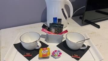 Una bandeja de desayuno con dos tazas blancas, una tetera blanca y diferentes paquetes de chocolate y té.