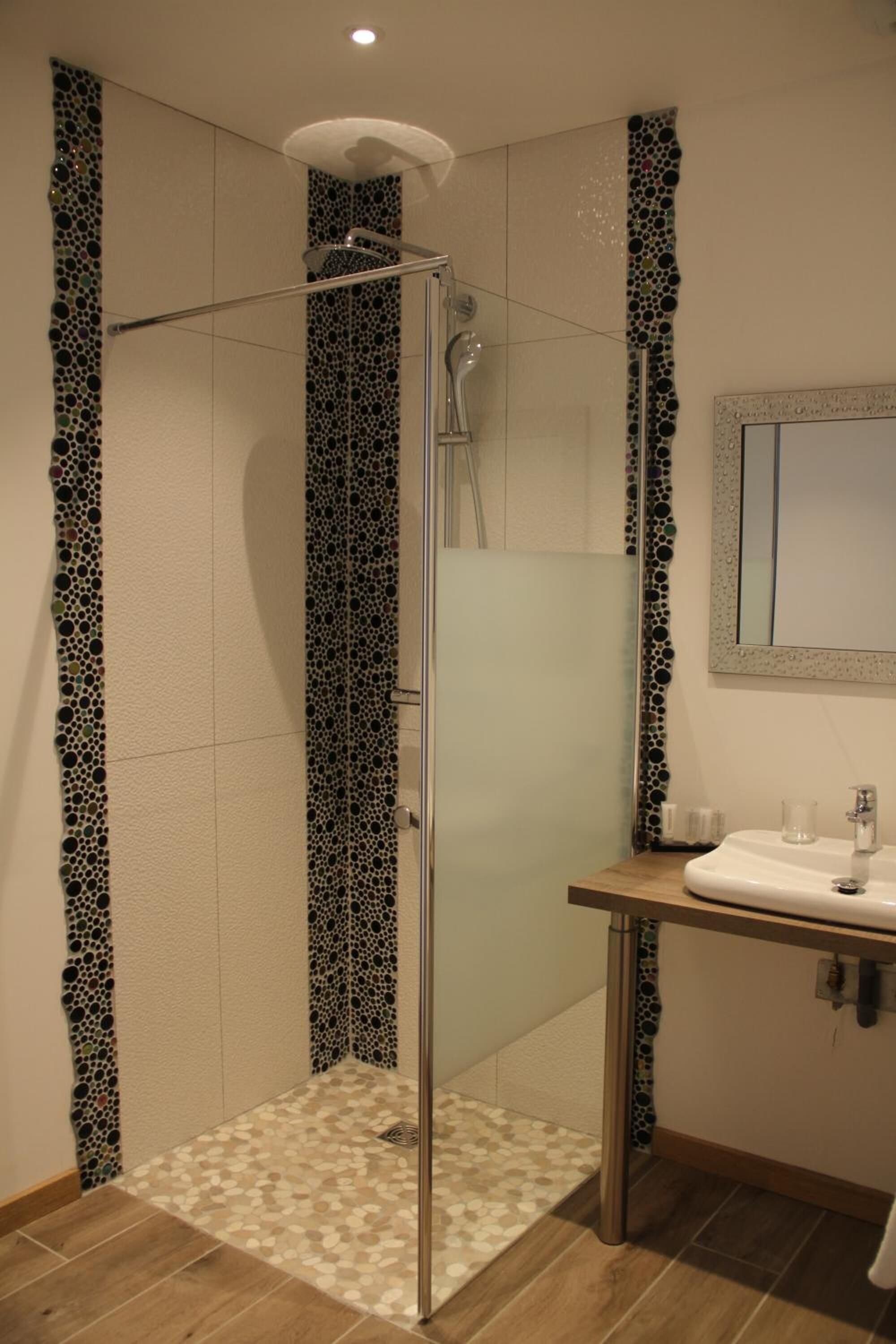 Een douche met glazen deur, een wastafel met spiegel, en betegelde muren en vloer.