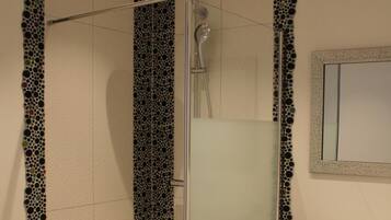 Een douche met glazen deur, een wastafel met spiegel, en betegelde muren en vloer.