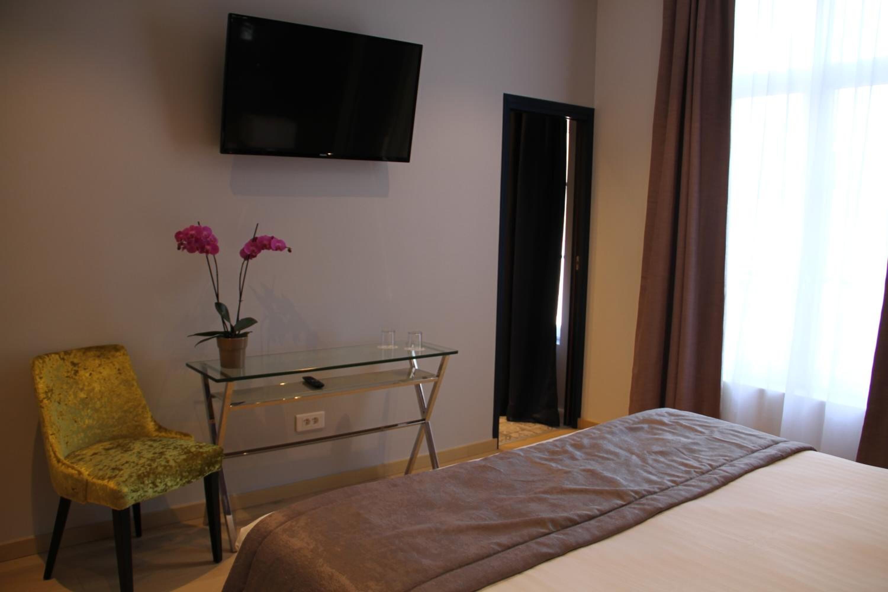 Une chambre d’hôtel comprenant un lit, un téléviseur fixé au mur, un bureau avec une chaise et une fenêtre avec des rideaux.
