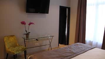 Une chambre d’hôtel comprenant un lit, un téléviseur fixé au mur, un bureau avec une chaise et une fenêtre avec des rideaux.