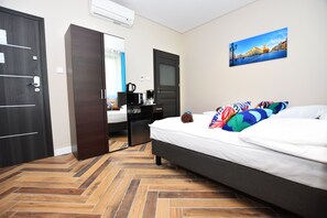 A hotel room with a bed, a desk with a chair, a wardrobe, and a painting on the wall. - DUKES Apartments - Old Town (Wroclaw)