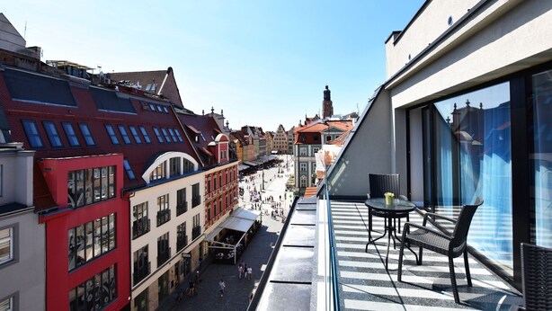 A narrow street with buildings on either side, a clear sky, and a balcony with outdoor seating. - DUKES Apartments - Old Town (Wroclaw)